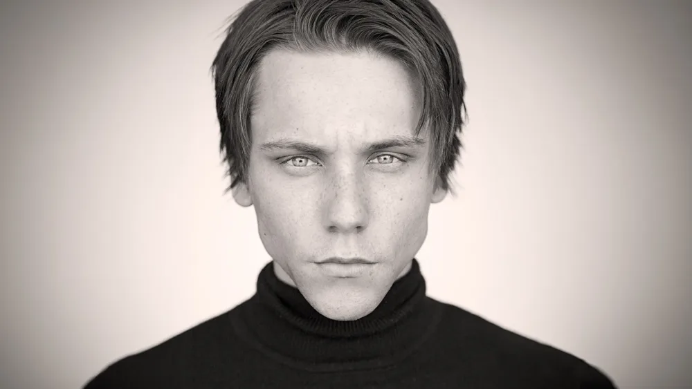 Dramatic black-and-white acting headshot of actor James Austin Kerr with tousled blond hair, wearing a black turtleneck against a soft gray background.