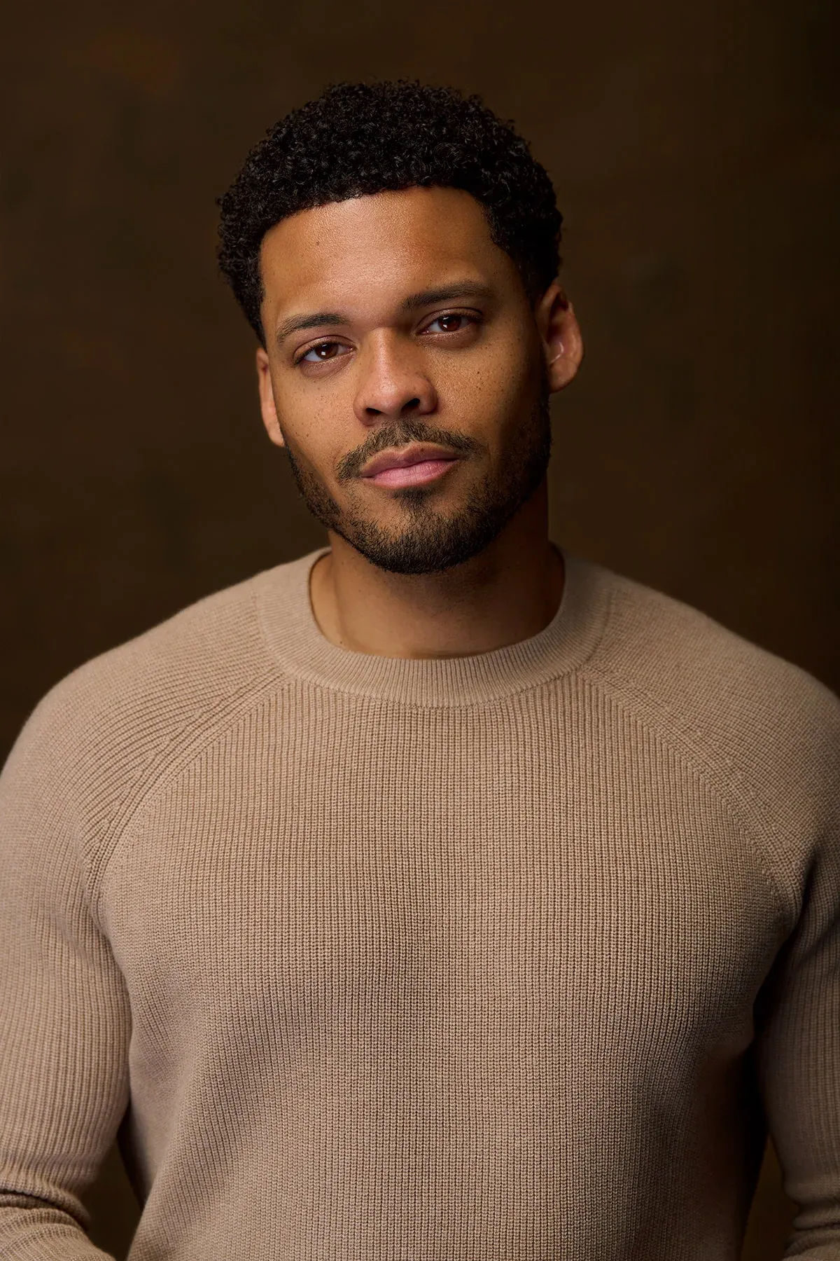 Deric Augustine in a taupe ribbed sweater on a warm brown backdrop — celebrity headshot by Headshots LA in Los Angeles.