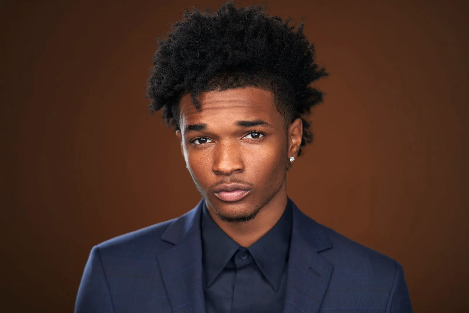 Isaiah Hill in a navy plaid suit on a warm brown backdrop — celebrity headshot by Headshots LA in Los Angeles.